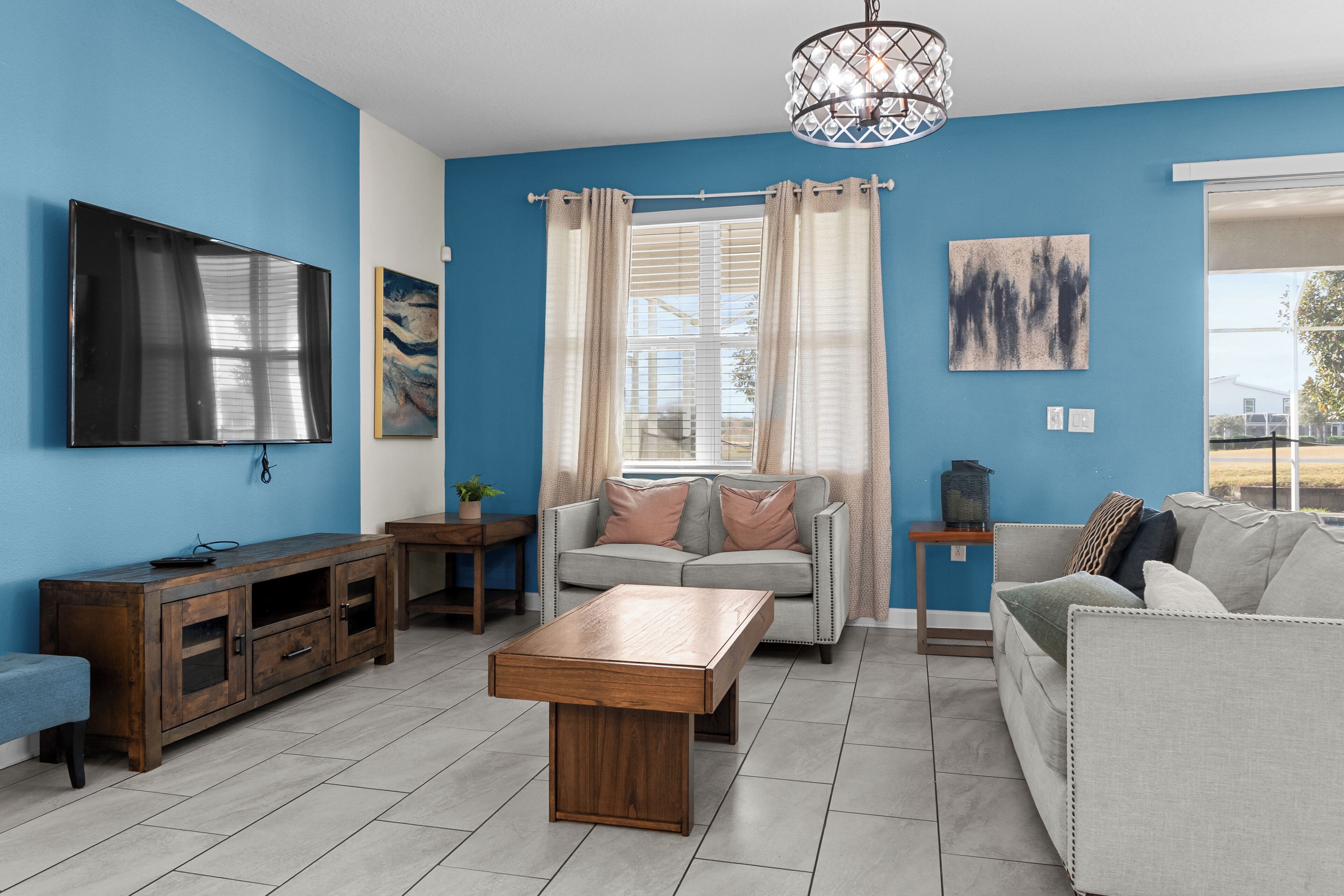 Ein Wohnzimmer mit blauer Wand, einem Flachbildfernseher, einem hölzernen Couchtisch, einem grauen Sofa und einem beigen Sofa.