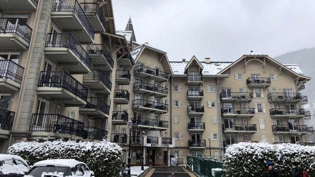 Ein mehrstöckiges Hotel mit Balkonen, einem mit Schnee bedeckten Dach und einer Bergkulisse.