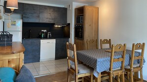 Eine kleine Küche mit modernen Geräten, ein Essbereich mit Holztischen und -stühlen sowie ein Deckenventilator.