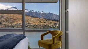 A room with a bed, a yellow armchair, and a large window offering a view of mountains and a lake.
