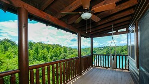Un terrazzo in legno con una ventola a soffitto, un'amaca e vista su un paesaggio boschivo.