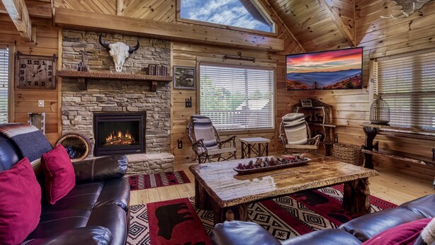 L’intérieur chaleureux d’un chalet avec une cheminée en pierre, des meubles en cuir et une grande fenêtre donnant sur un paysage magnifique.