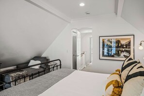A bedroom with a bed, a chair, a small table, and a framed picture on the wall.