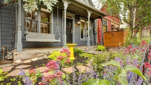 Een huis met een veranda, een schommel en een tuin met verschillende planten en bloemen.