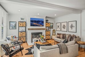 A modern living room with a fireplace, a mounted TV, and a collection of framed artwork. - Abode at Watson House, private hot tub, walk to town lift & Main Street (Park City)