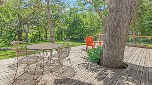 Una terraza de madera con una mesa y sillas, rodeada de árboles.