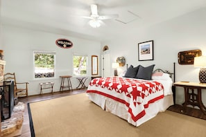 A bedroom with a bed, a ceiling fan, a welcome sign, a framed picture, and a window with a view of greenery.