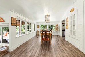 A spacious room with a wooden dining table and chairs, large windows, and a view of the outdoors.