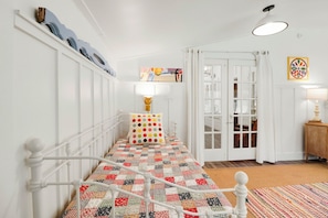 A hallway with a white bed, a patterned rug, a door with glass panels, and a wall-mounted lamp.
