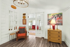 A room with a wooden floor, a red chair, a wooden dresser, and a painting on the wall.