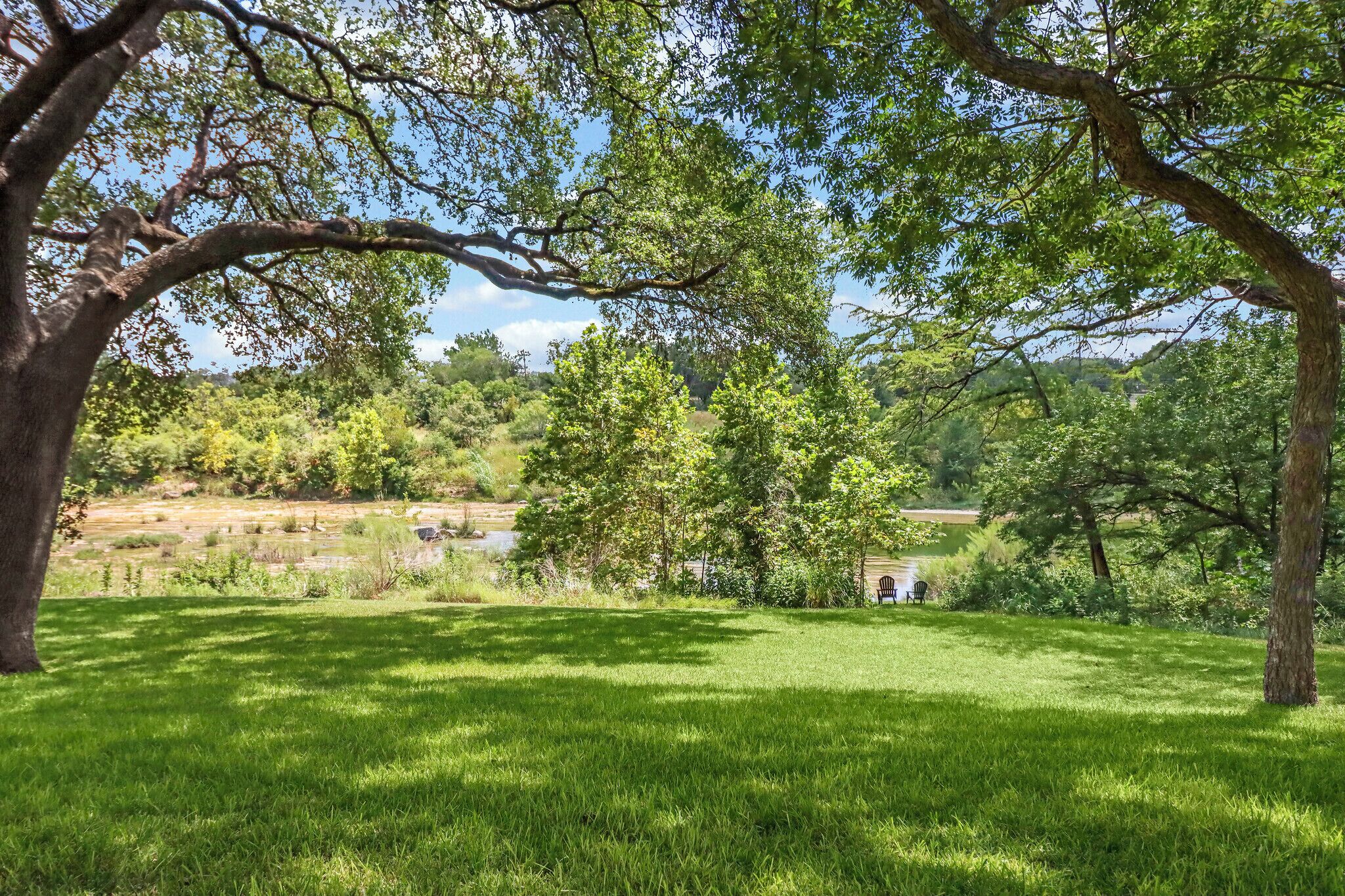 A grassy field with trees and a small building in the distance.