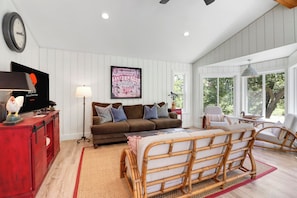 A living room with a brown sofa, a red cabinet, a television, and a large window with a view of trees.