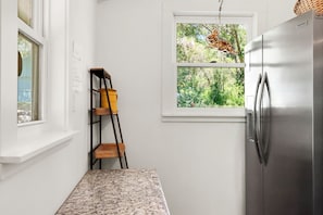 A kitchen with a stainless steel refrigerator, a window with a view of greenery, and a wooden ladder against the wall.