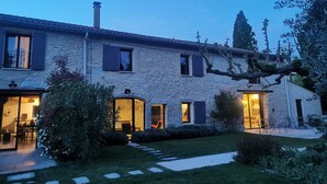Una casa de piedra con varias ventanas, una chimenea visible y un jardín bien cuidado con losetas que guían al acceso.