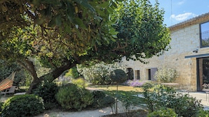 Un jardín con un sendero de grava, diversos arbustos y un árbol grande que da sombra.