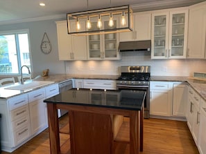 A modern kitchen with white cabinetry, a black countertop, a stainless steel stove, and a pendant light fixture.