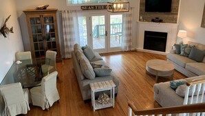 A living room with a glass table, two sofas, a fireplace, and a TV mounted on the wall. - Tortuga: Spacious 5-bedroom home in Holden Beach, perfect for family fun! (Holden Beach)