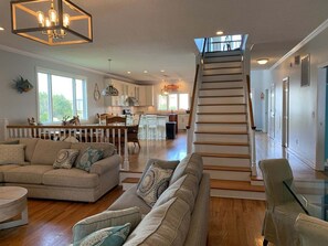 A spacious living area with a staircase leading to an upper floor, a dining area, and a kitchen. - Tortuga: Spacious 5-bedroom home in Holden Beach, perfect for family fun! (Holden Beach)