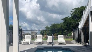 A swimming pool with a tiled edge, surrounded by white lounge chairs and a metal fence. - Tortuga: Spacious 5-bedroom home in Holden Beach, perfect for family fun! (Holden Beach)