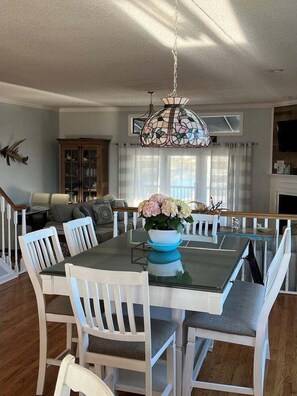 A dining area with a glass table, white chairs, a floral centerpiece, and a stained glass chandelier.