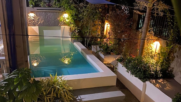 Ein Schwimmbecken mit Stufen zum Wasser, umgeben von Pflanzen und einem schattigen Bereich.