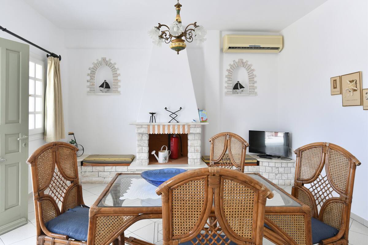 A dining area with wicker chairs, a glass table, a fireplace, and a television.