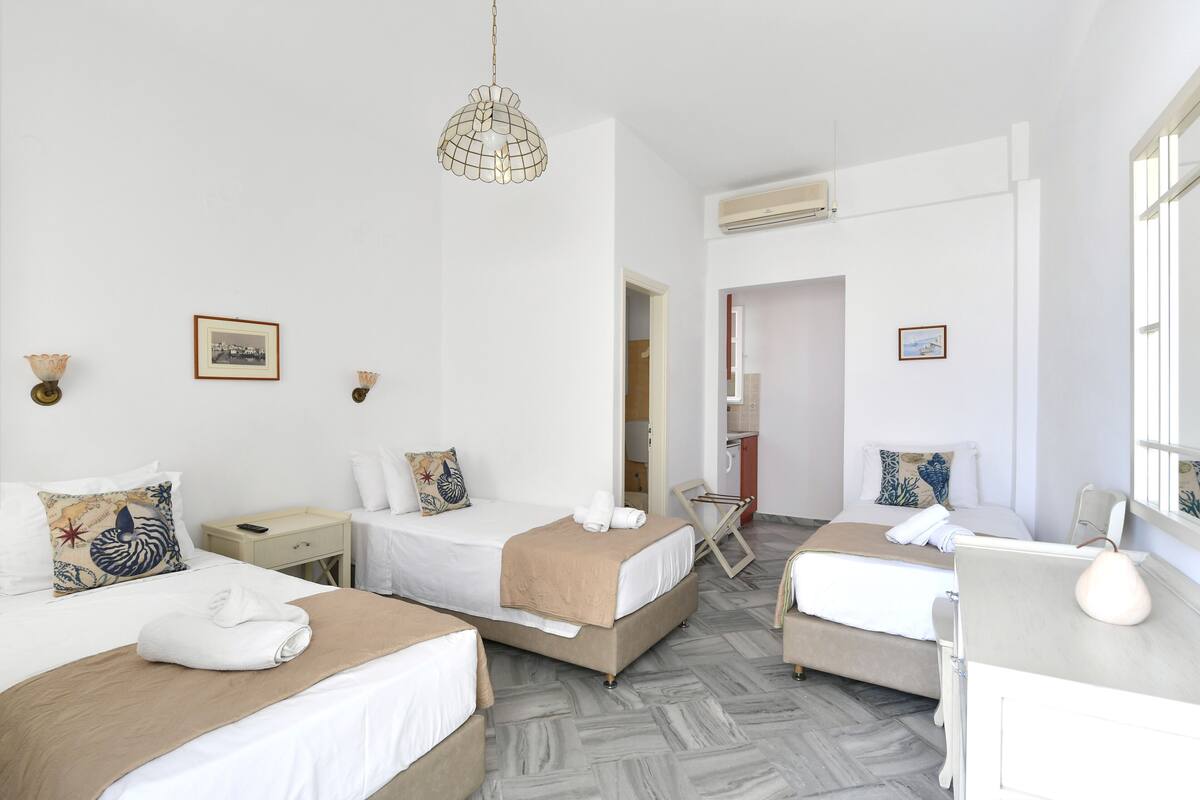 A hotel room with two beds, a desk, and a chair. There are framed pictures on the walls and a hanging light fixture.
