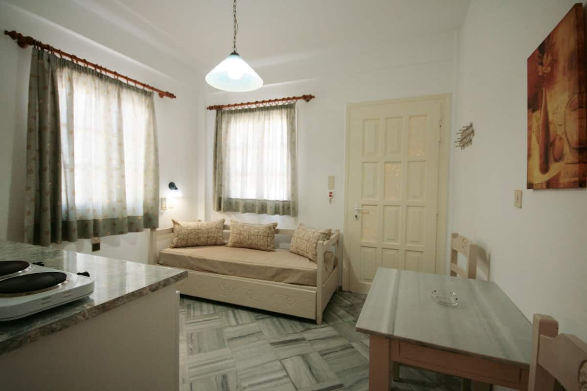 A small, well-lit room with a bed, a table, and a chair.