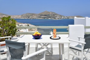 A table with a bowl of fruit and a tray with glasses and a drink, overlooking a coastal landscape with mountains and the sea.