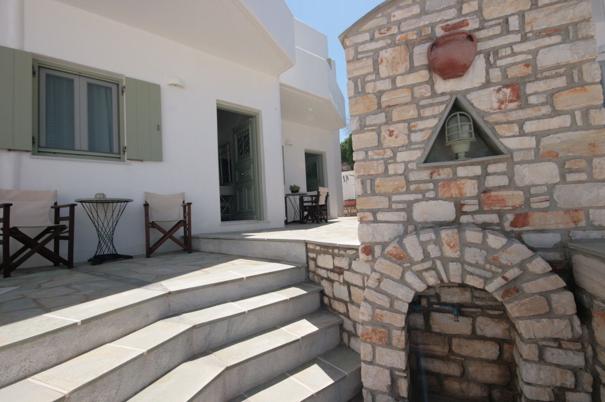 A stone staircase leading to a door, a small table with chairs, and a stone wall with a decorative element.