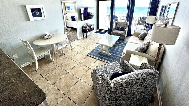A hotel room with a balcony, a bed, a TV, a dining table, and a sofa.