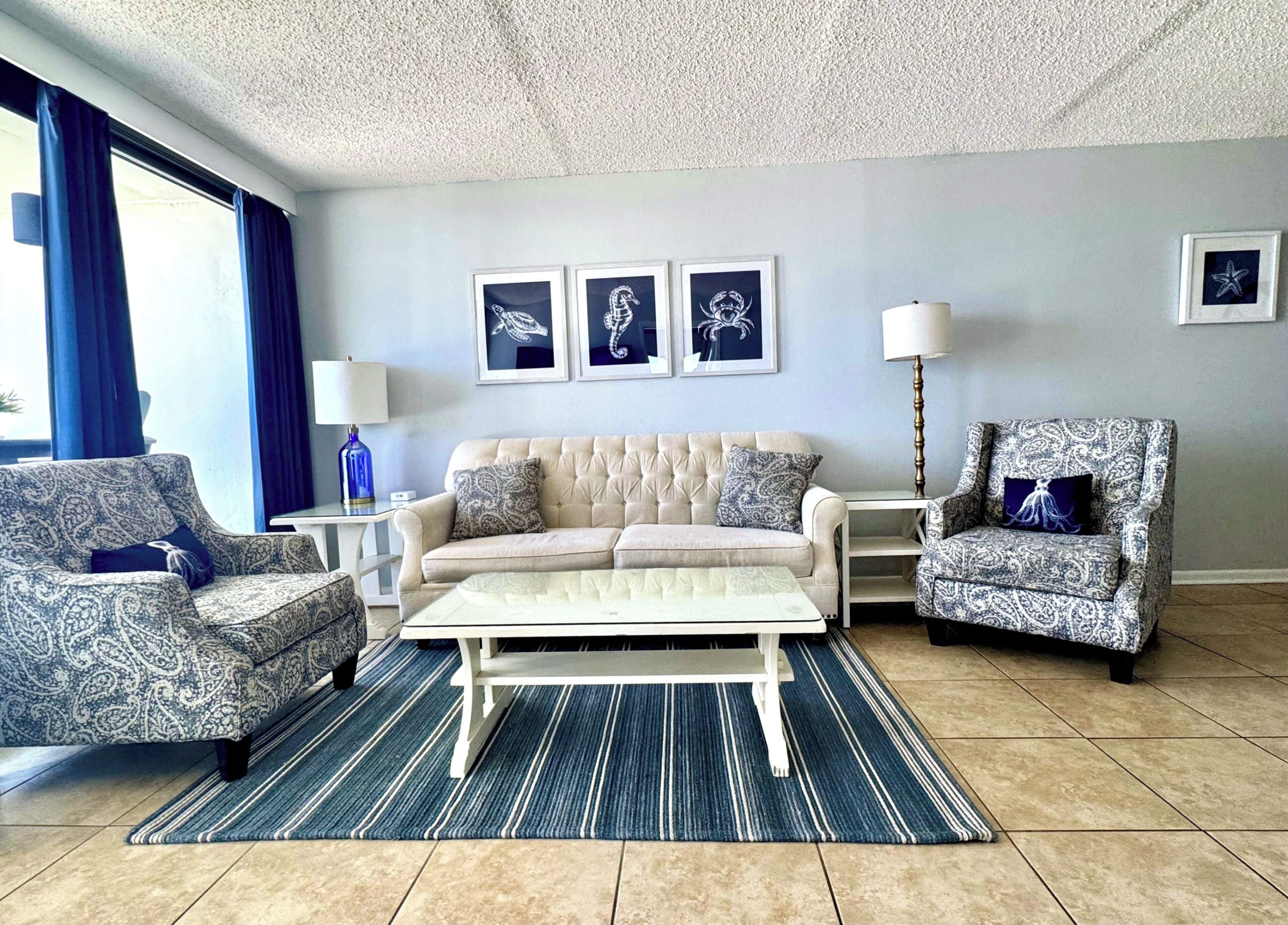 A living room with a beige sofa, patterned armchairs, a coffee table, and framed artwork on the wall.