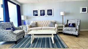 A living room with a beige sofa, patterned armchairs, a coffee table, and framed artwork on the wall.