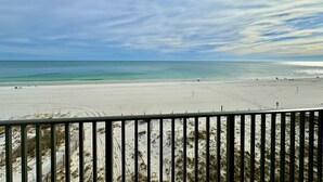 A beach view from a balcony with a railing, sandy beach, and ocean.