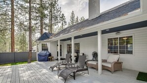 A covered deck with outdoor furniture, a grill, and a view of tall trees.