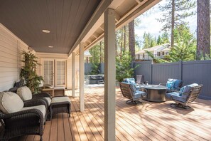A covered patio area with wicker furniture, a round table, and a view of a residential neighborhood with trees and houses.