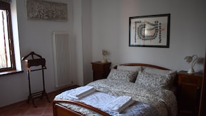 A bedroom with a wooden bed, a radiator, a framed artwork, and a bedside table with a lamp.