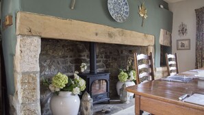 A dining room with a stone fireplace, wooden chairs, a table, and decorative items. - Forthay Bed and Breakfast (Dursley)