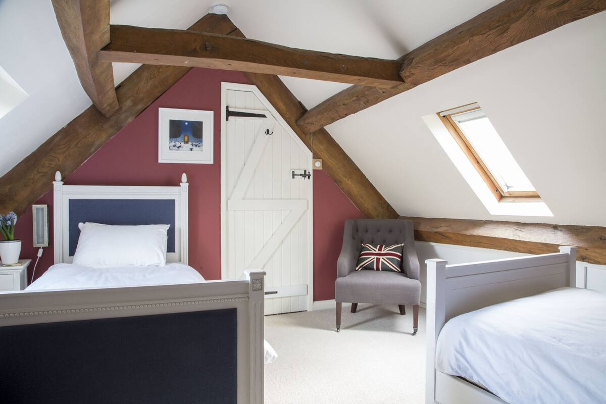 A bedroom with a sloped ceiling, a bed, a chair, and a door.