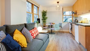 A modern living room with a grey sofa, a dining area with a table and chairs, and a kitchen with wooden cabinets and a dishwasher. - Griffith Rooms (Dublin)