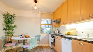 A modern kitchen with wooden cabinets, a white dishwasher, and a dining area with a round table and chairs. - Griffith Rooms (Dublin)