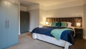 A bedroom with a large bed, a wardrobe, a bedside table with a lamp, and a nightstand. - Griffith Rooms (Dublin)