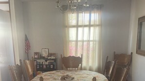 Une salle à manger avec une table ronde, des chaises en bois, un lustre et une fenêtre avec des rideaux.