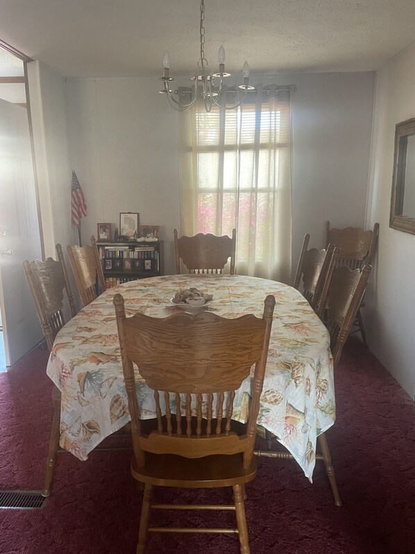A dining room with a round table, wooden chairs, a chandelier, and a window with curtains. - Fishing/ Beach Getaway (Holden Beach)