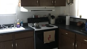 Une cuisine avec des meubles de rangement en bois, une cuisinière, un évier et une fenêtre avec des rideaux.