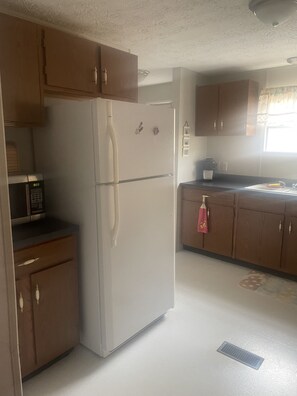 A kitchen with wooden cabinets, a white refrigerator, a microwave, and a sink. - Fishing/ Beach Getaway (Holden Beach)