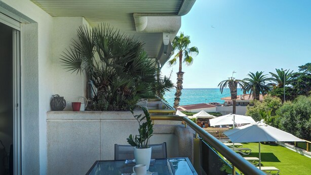 A balcony with a glass table, chairs, and a potted plant. There are palm trees and a view of the ocean. - Mediterraneo Seaview by Hello Homes Sitges (Sitges)