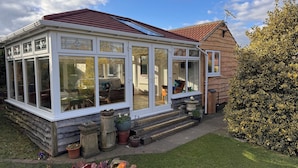 A conservatory with a glass roof, wooden exterior, and a garden area with potted plants. - Gardenside Lodge self - catering dog friendly holiday home in County Durham (County Durham)