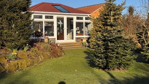 A house with a red roof, a glass conservatory, and a well-maintained garden with various plants and a small Christmas tree. - Gardenside Lodge self - catering dog friendly holiday home in County Durham (County Durham)
