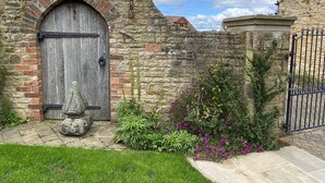 A rustic stone building with a wooden door, a stone wall, and a metal gate. - Gardenside Lodge self - catering dog friendly holiday home in County Durham (County Durham)